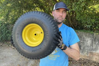 Dave Greenwood holding a John Deere lawn tractor rear tire and wheel